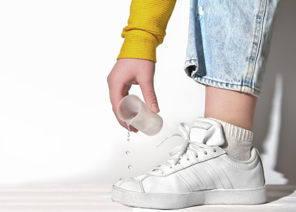 female hand pouring water on a white sneakers.