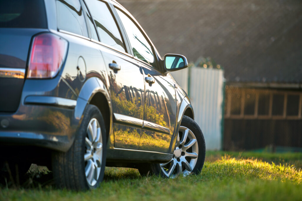 New shiny gray car parked on green grass on blurred sunny summer rural background